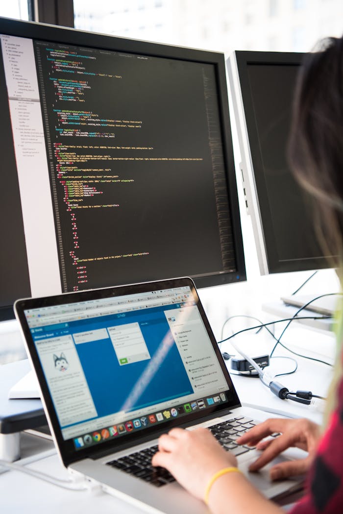 Services Programmer working on code across multiple screens in a modern office setting.