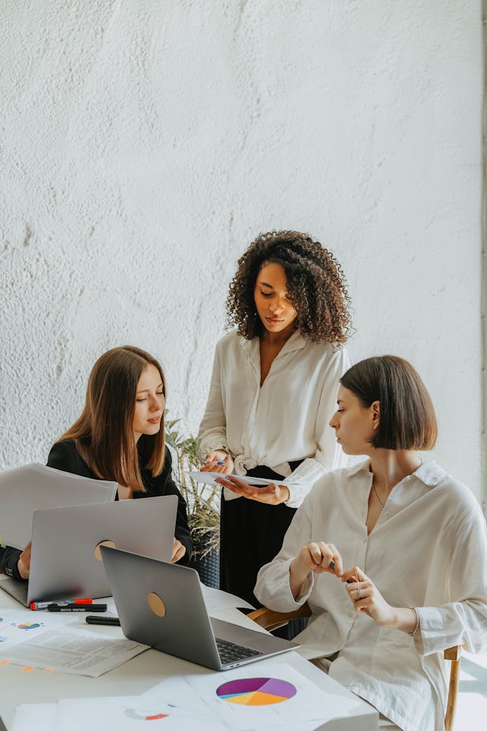 Services Three women collaborate on a project with charts and laptops in an office.